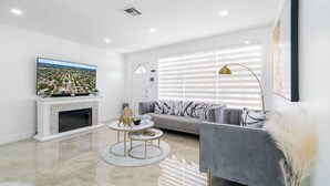 A modern living room with a flat-screen TV, a fireplace, a sofa, and a round coffee table. - Stunning Home with a HEATED POOL 4 miles to the beach! (Pompano Beach)