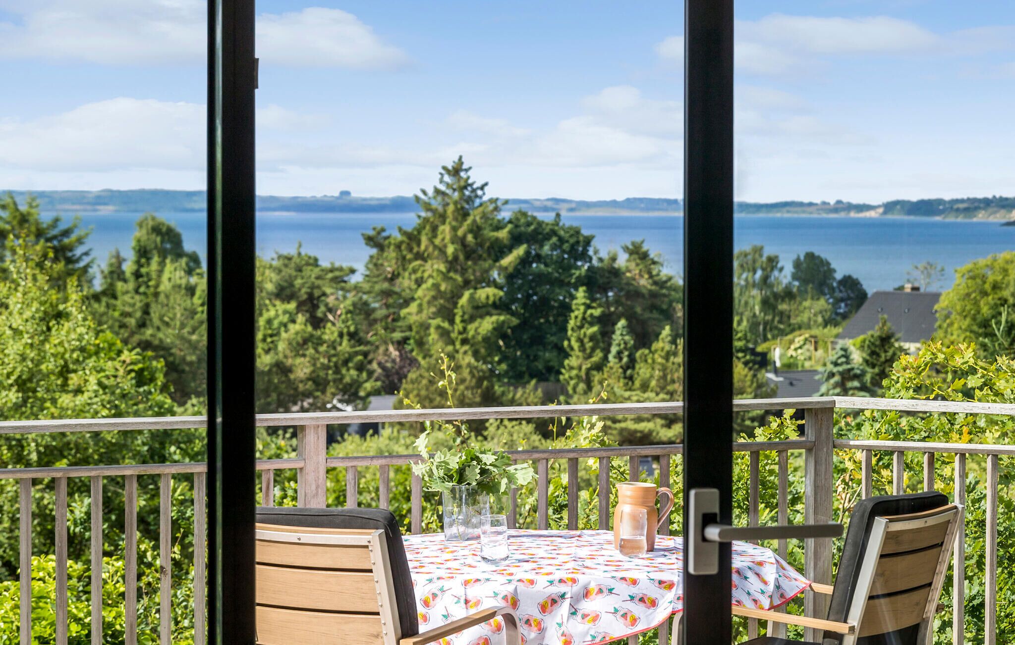 Un balcon avec une table dressée pour deux personnes, offrant une vue panoramique sur un lac et une forêt.