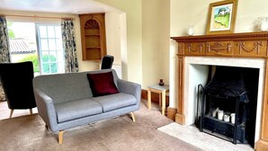 Ein Wohnzimmer mit grauem Sofa, Kamin und einem Fenster mit Vorhängen.