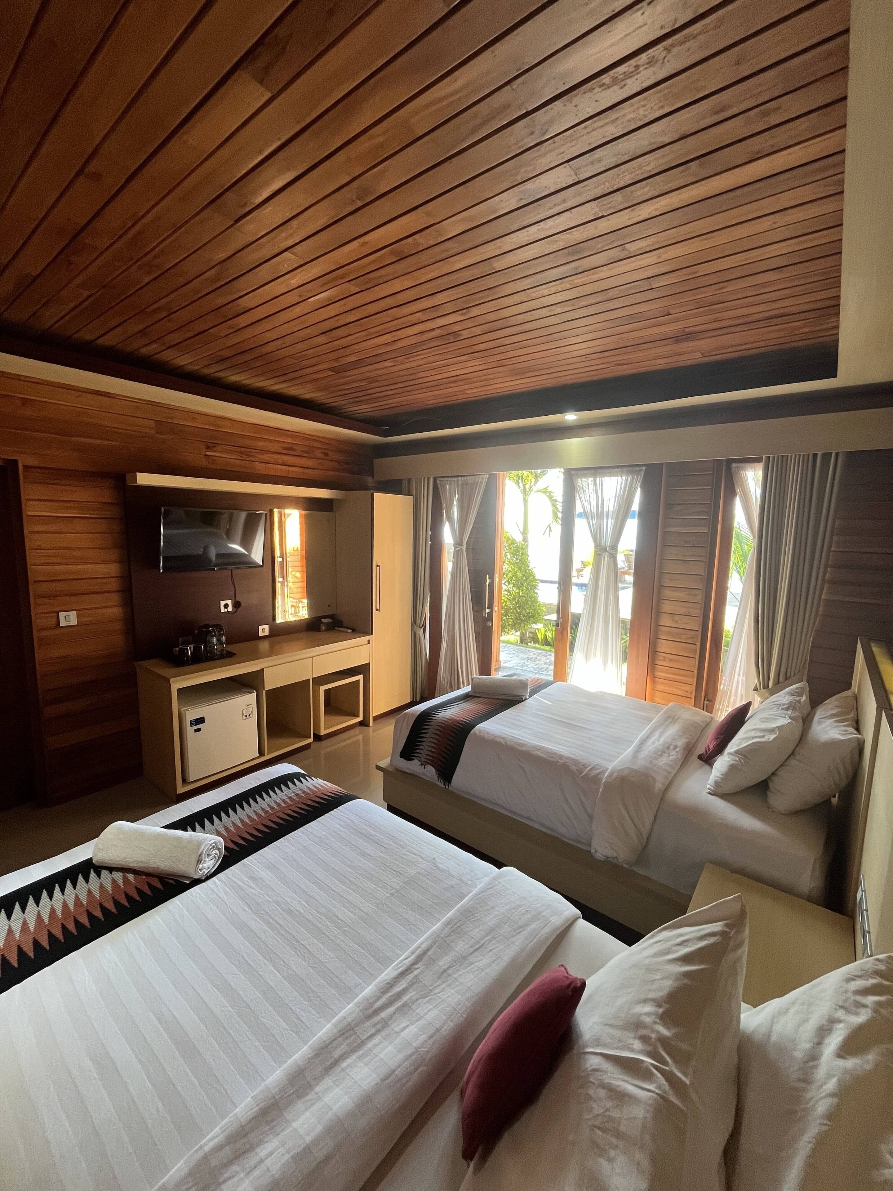 Ein Hotelzimmer mit zwei Betten, einem Fernseher, einem Schreibtisch und Blick ins Freie.