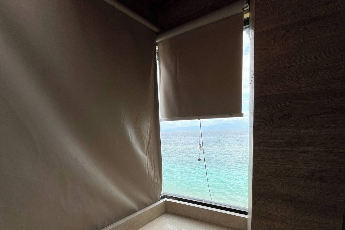 Un coin de pièce avec une baignoire, une fenêtre donnant sur la mer et des poutres en bois au plafond.