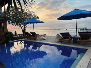 Un espace aménagé au bord de la piscine, avec des chaises longues et des parasols, offrant une vue sur l’océan.