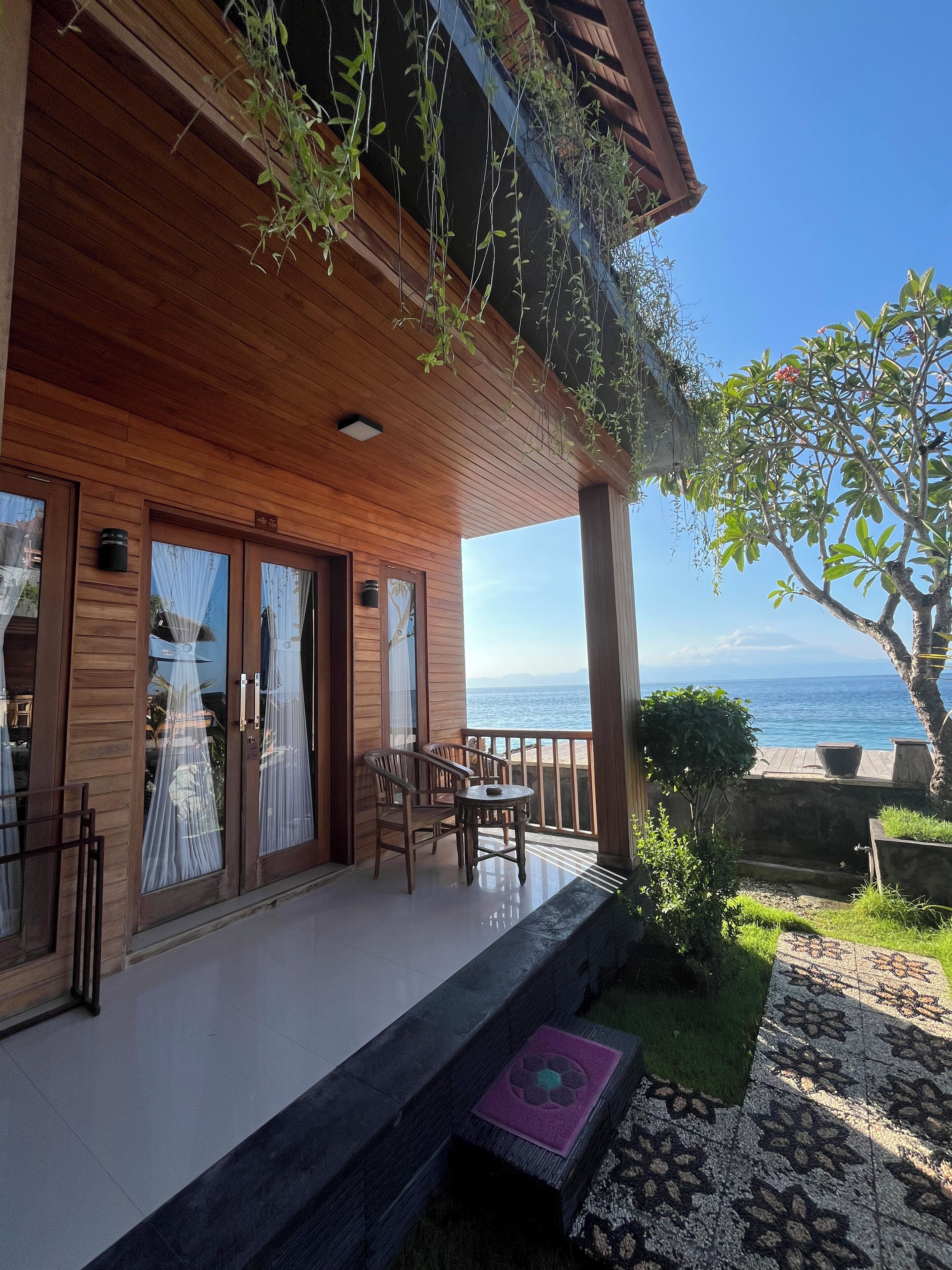 Un terrazzo in legno con vista sul mare, un tavolo e sedie, e un piccolo giardino.