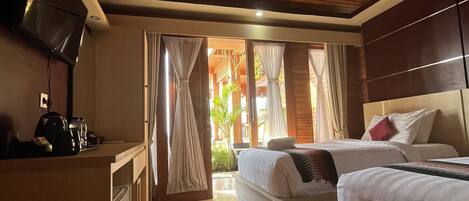 A hotel room with a wooden ceiling, a TV mounted on the wall, a bed with white bedding, and a small kitchenette area.