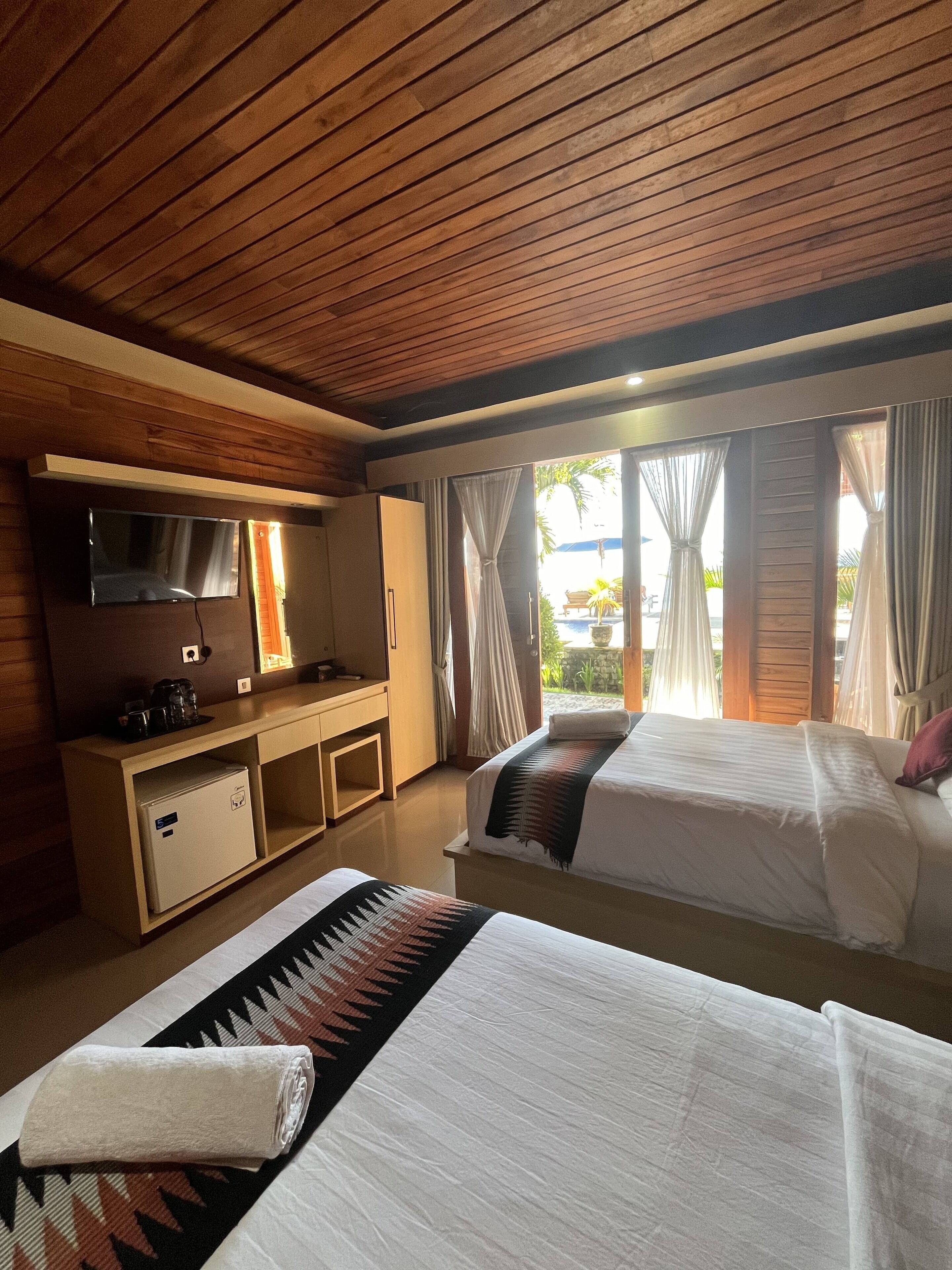 Habitación de hotel con dos camas, un escritorio, un televisor y vistas al exterior.