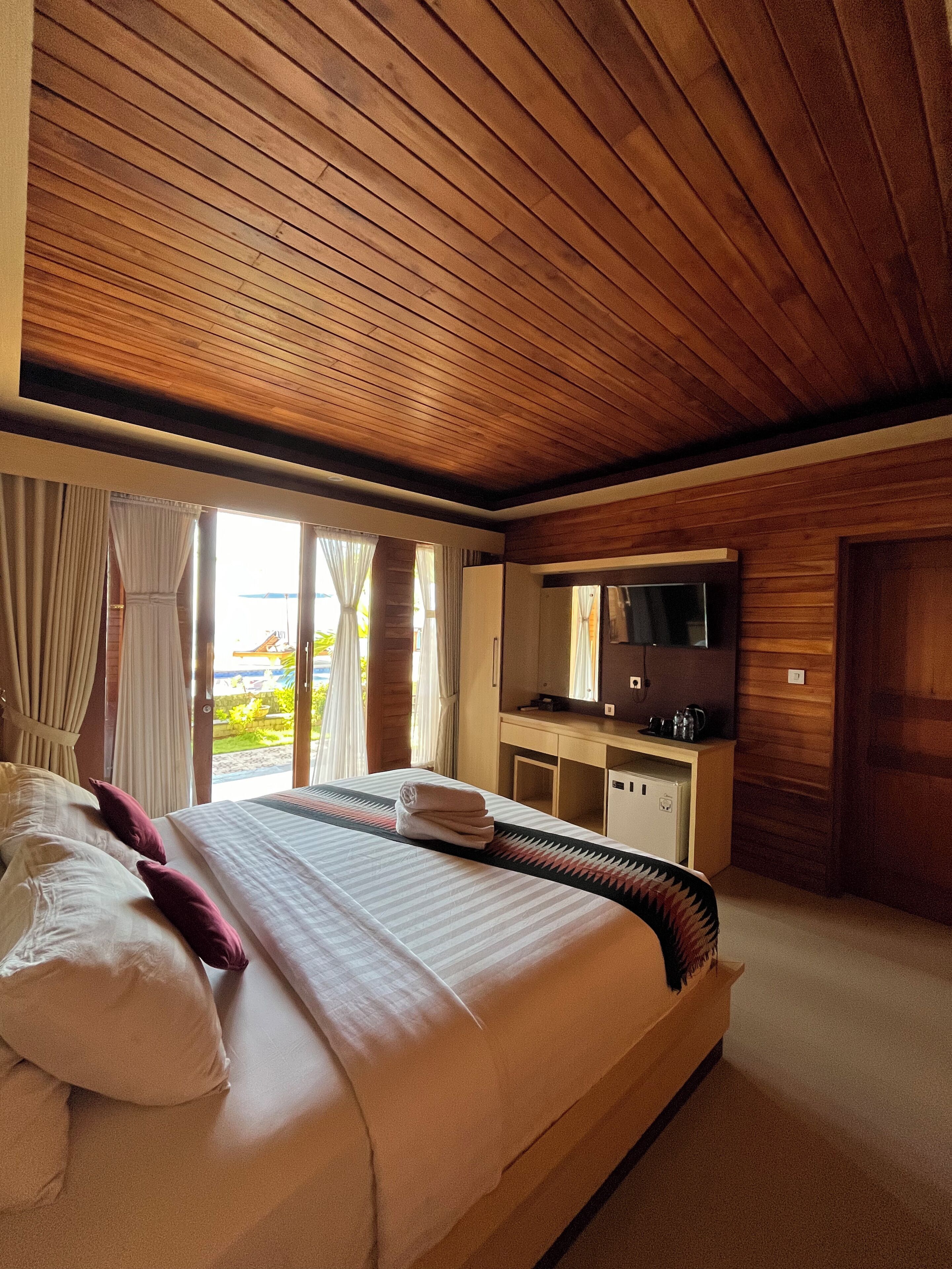 A hotel room with a large bed, a desk with a TV, and a view of the beach.