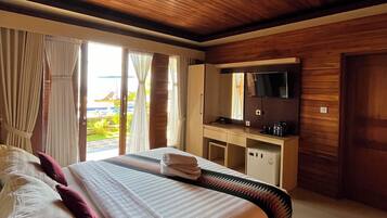 A hotel room with a large bed, a desk with a TV, and a view of the beach.