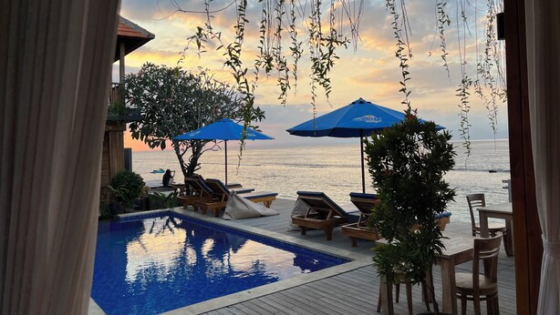 Evigheds-pool med liggestole og parasoller med udsigt over vand ved solnedgang.