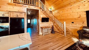 Eine geräumige Holzhütte mit einer zentralen Treppe, einer Küchenzeile und einer gemütlichen Sitzecke.