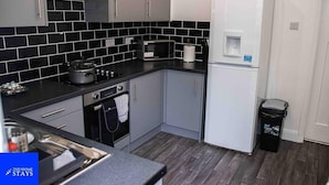A compact kitchen with grey cabinets, a black tiled backsplash, a microwave, a kettle, and a white refrigerator. - Stoke House Sleeps 5 with Garden and Parking (Stoke-on-Trent)