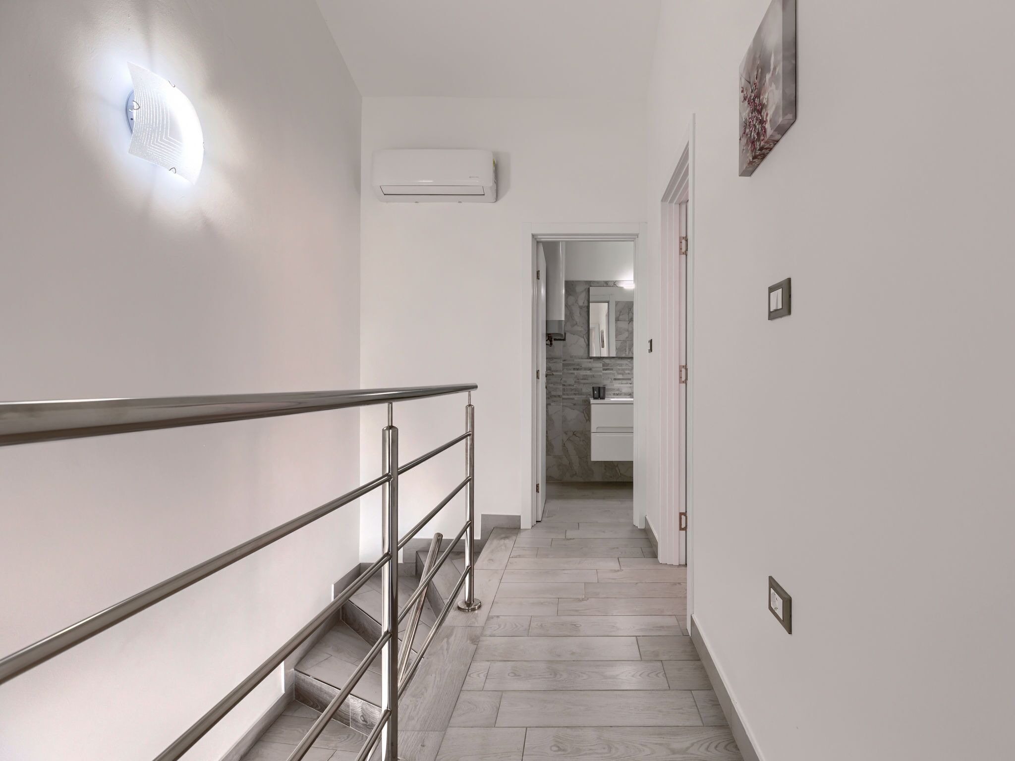 A modern hallway with a staircase, a wall-mounted air conditioner, and a door leading to a bathroom.