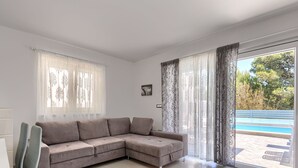 A modern living room with a beige sectional sofa, a dining table with chairs, and a large sliding glass door leading to a pool. - Villa Oli/A by Interhome (Medulin/Ližnjan)