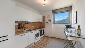Eine moderne Küche mit Waschmaschine, ein Essbereich mit Tisch und Stühlen sowie ein Fenster mit Blick auf die Berge.