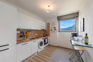 Uma cozinha moderna com máquina de lavar, uma área de refeições com mesa e cadeiras, e uma janela com vista para as montanhas.