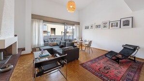 Ein modernes Wohnzimmer mit einer Couch, einem Couchtisch, einem roten Teppich mit Muster, einem schwarzen Sessel und einem Kamin.