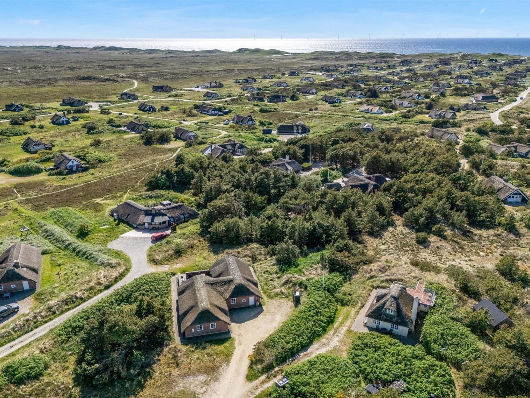 Vista aérea de un pueblo costero con casas rodeadas de vegetación y una vista despejada del mar.