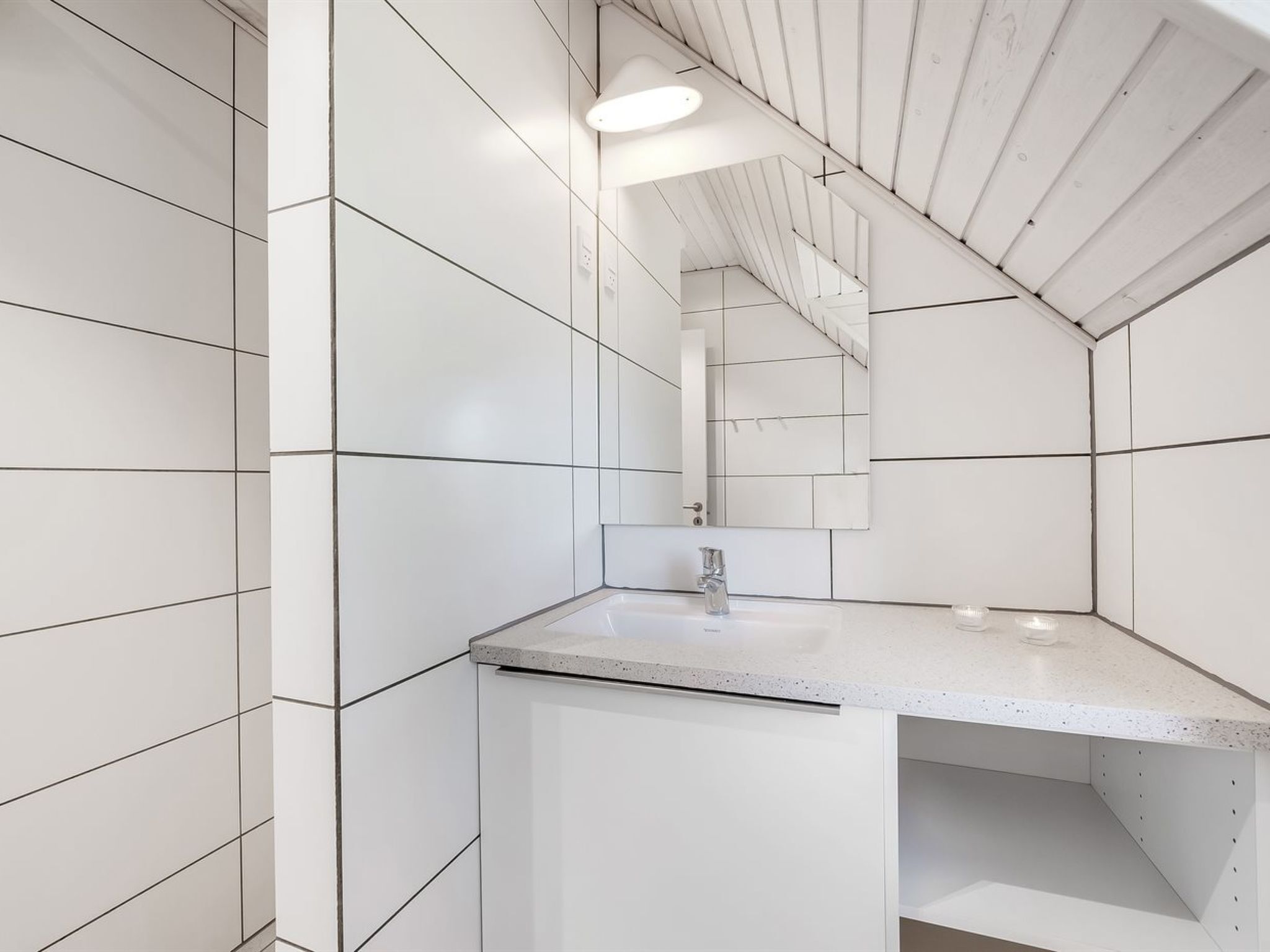 A modern bathroom with white tiles, a sink, and a mirror.