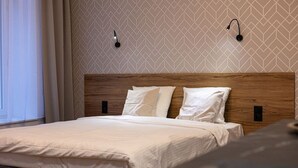 Una cama bien hecha con cabecera de madera, dos lámparas de noche y un papel tapiz estampado.