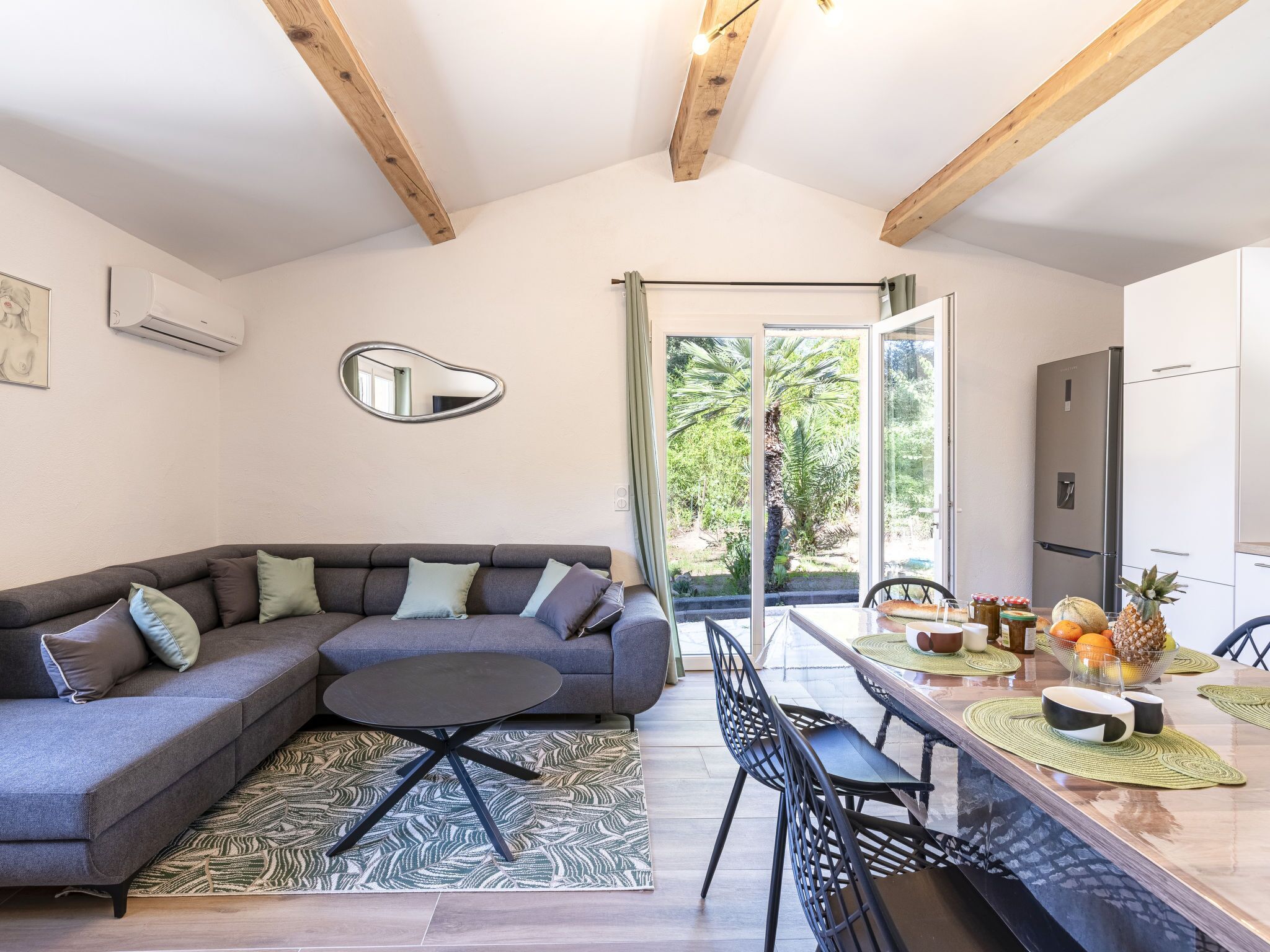 Un salon moderne avec un canapé d’angle gris, une petite table ronde et un coin repas comprenant une table et des chaises en bois.