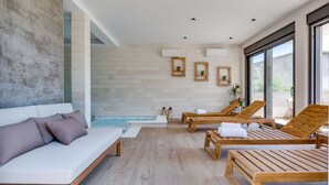 Un área de spa moderna con un sofá blanco, sillones de madera, una pequeña piscina y cuadros enmarcados en la pared.