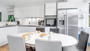 Eine moderne Küche mit weißen Schränken, einem Edelstahlkühlschrank und einem Essbereich mit rundem Tisch und Stühlen.