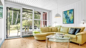 Ein modernes Wohnzimmer mit einem gelben Ledersofa, einem Glastisch und einem großen Fenster mit Blick auf Grünflächen.