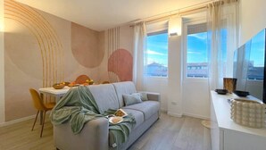 A modern living room with a grey sofa, a dining table with chairs, and a kitchen area with a white countertop. - Nystrom Apt - Self Check-in - Metro M1 (Milano)