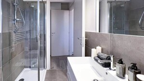 A modern bathroom with a glass-enclosed shower, a white sink with a large mirror, and a towel rack with towels. - Nystrom Apt - Self Check-in - Metro M1 (Milano)