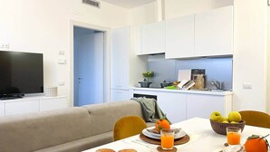A modern living room with a sofa, a dining table set with breakfast, and a kitchen in the background. - Nystrom Apt - Self Check-in - Metro M1 (Milano)