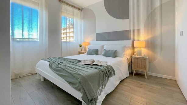 A modern bedroom with a large bed, bedside lamps, and a view of the outdoors through sheer curtains. - Nystrom Apt - Self Check-in - Metro M1 (Milano)