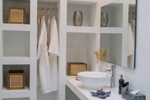 Une salle de bain moderne avec un grand lavabo blanc, un miroir et des étagères où sont rangées des serviettes et des objets décoratifs.