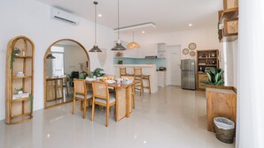 A modern kitchen with a central island, wooden chairs, and pendant lighting. - Villa Noni Kerobokan (Seminyak)
