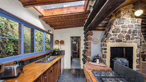 Una cocina rústica con chimenea de piedra, armarios de madera y un amplio ventanal con vistas al follaje.