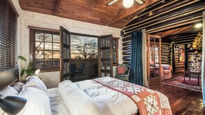 Un dormitorio rústico de madera con una cama grande, una mesita de noche, una lámpara y vistas al exterior.