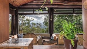 Una habitación acogedora con techo de madera, ventanas amplias, un piano, una mesa con un tablero de ajedrez y una planta en maceta.