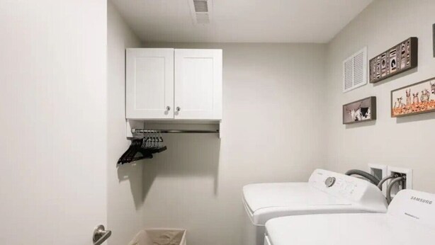A small, clean room with a white wardrobe, two white washing machines, and a wall-mounted shelf with shoes.