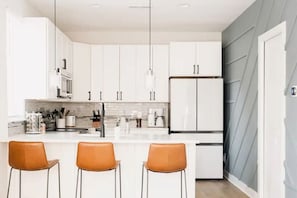 Una cocina moderna con armarios blancos, una isla central con taburetes y una lámpara colgante.