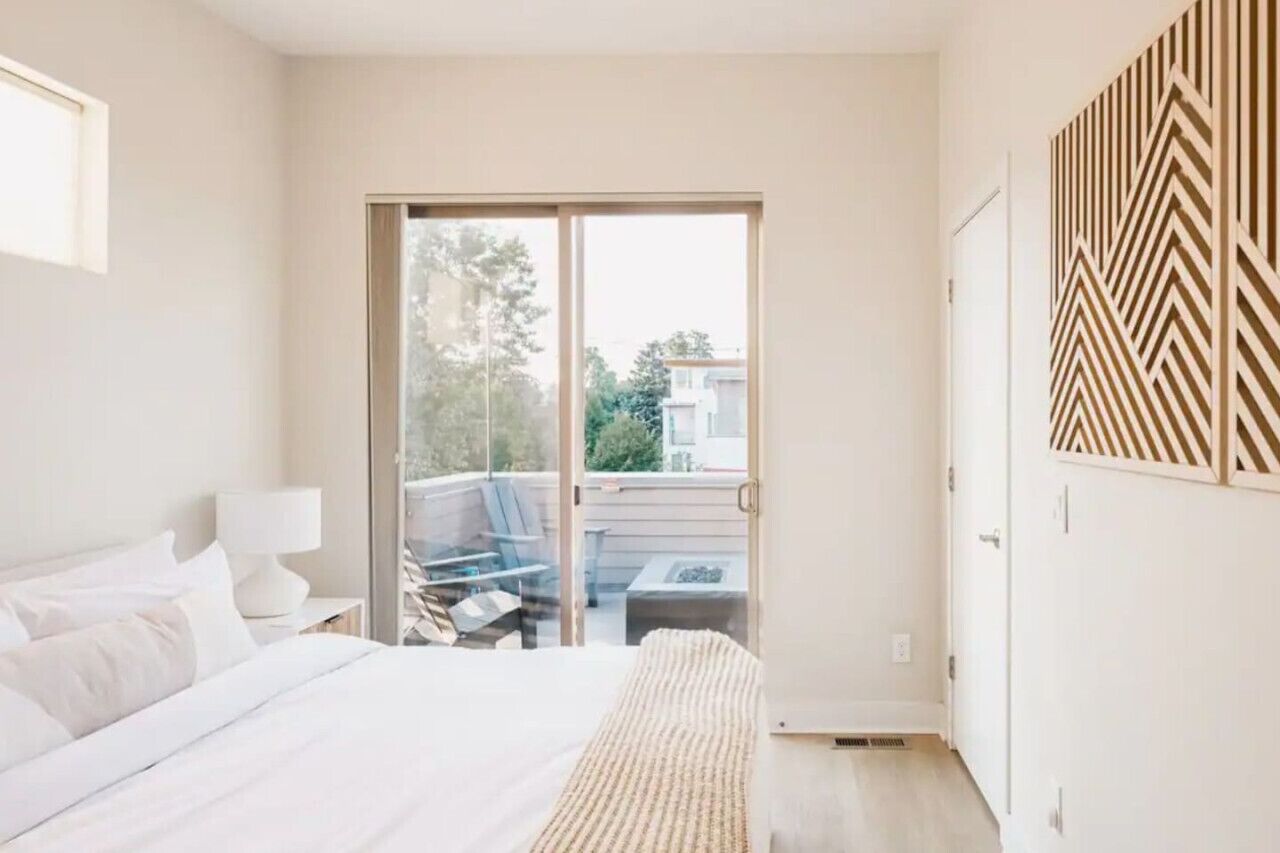 Une chambre à coucher comprenant un lit, une table de chevet, une lampe, une porte-fenêtre coulissante donnant sur un espace extérieur et un mur décoré d’un motif.