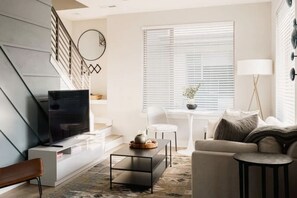 A modern living room with a flat-screen TV, a sofa, a coffee table, and a staircase.