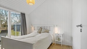 A bedroom with a white bed, a nightstand, and a window with curtains. - 5 bedroom nice home in Græsted (Græsted)