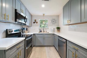 Une cuisine moderne avec des meubles gris, des appareils en acier inoxydable et un plan de travail blanc.