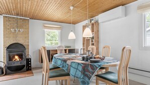 A cozy dining area with a brick fireplace, wooden ceiling, and a table set for four with chairs.