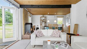 A modern living room with a fireplace, white sofas, a dining area, and a view of the outdoors.