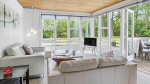 A modern living room with a large TV, white sofas, and a wooden ceiling.
