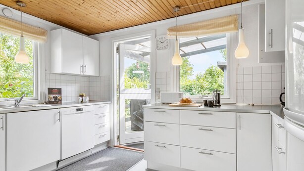 A modern kitchen with white cabinets, a wooden ceiling, and pendant lights.