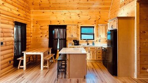 Ein Holzblockhaus-Interieur mit Küchenbereich, Holzboden, einem Esstisch mit Bänken und einer integrierten Bar.