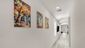 A hallway with three large paintings on the wall, a ceiling light, and a door at the end.