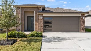 A modern two-story house with a garage, a small front yard with a tree, and a clear sky.
