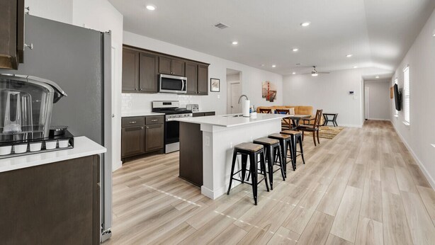 A modern kitchen with a central island, dark cabinets, and a dining area with a table and chairs.