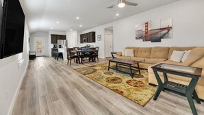 A spacious living area with a wooden floor, a beige sofa, a coffee table, and a dining area with a table and chairs.
